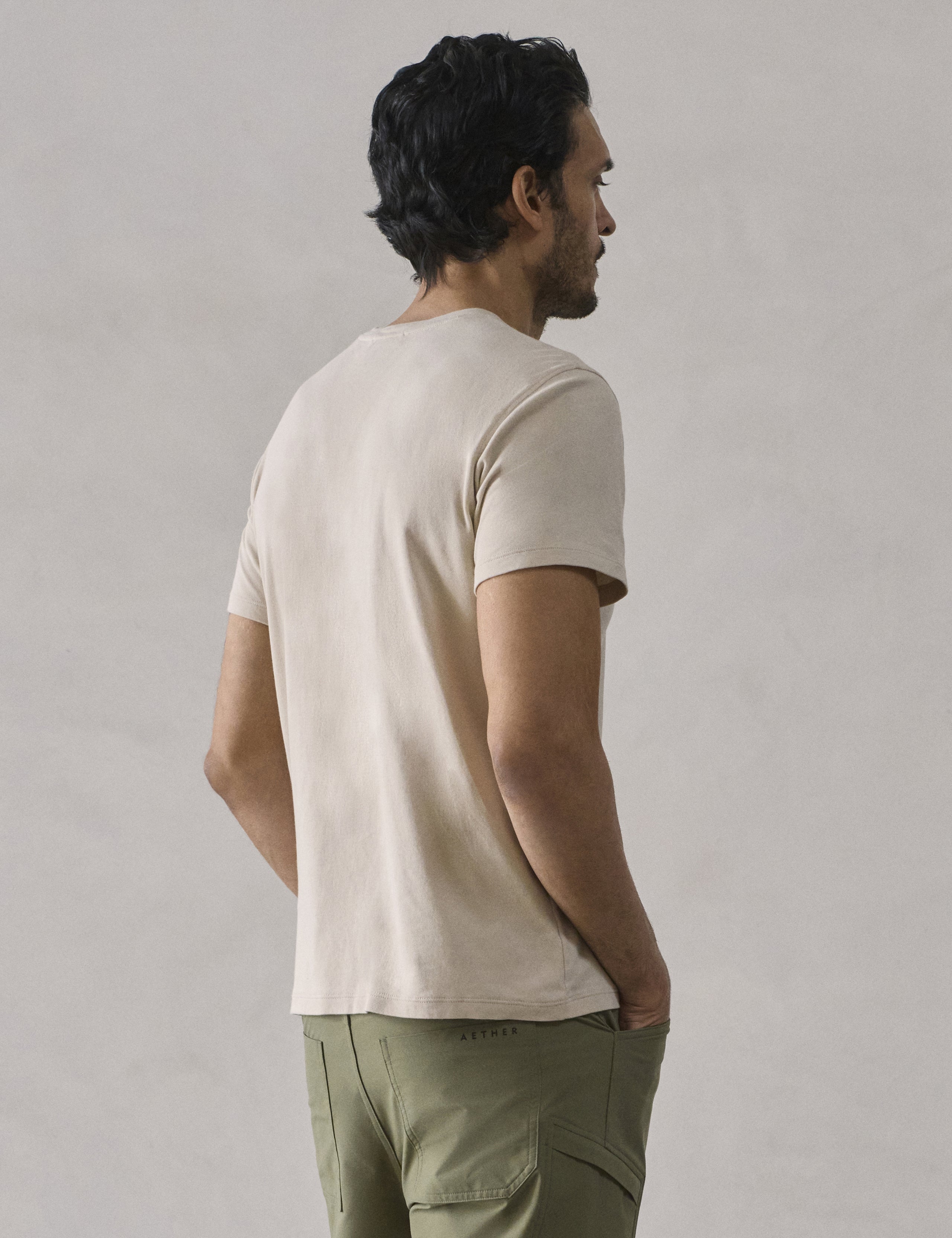 Rear 3/4 view of man wearing Emery Pima Crew Tee in Bone white from AETHER Apparel.